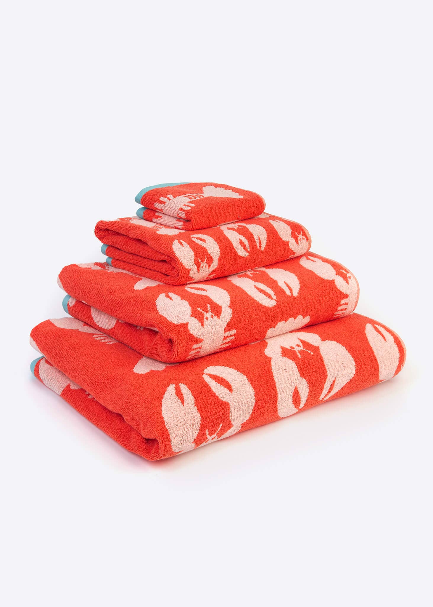 Stack of coral towels with white lobster patterns on a white background. 100% organic cotton and great house warming gift.